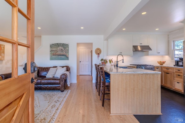 kitchen featuring stainless steel gas range oven, under cabinet range hood, light stone countertops, a breakfast bar area, and a sink