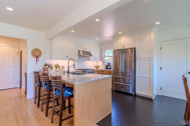 kitchen with a peninsula, white cabinetry, under cabinet range hood, a kitchen bar, and high end refrigerator