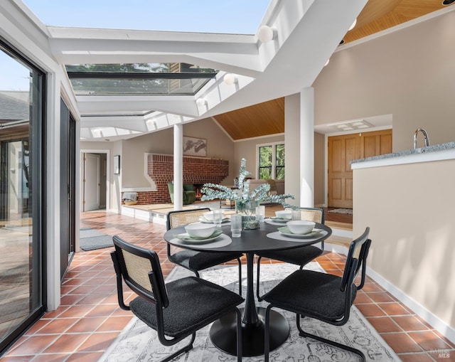 dining space with a skylight, high vaulted ceiling, light tile patterned flooring, and baseboards