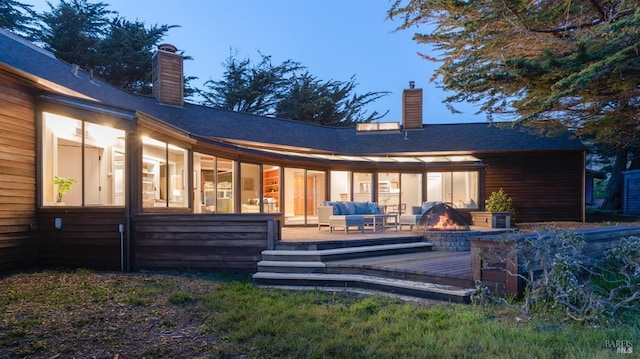 rear view of property featuring an outdoor living space with a fire pit, a wooden deck, and a chimney