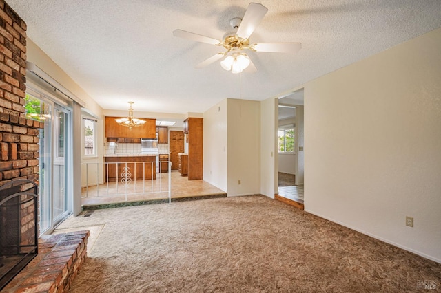 unfurnished living room with a textured ceiling, light colored carpet, ceiling fan with notable chandelier, and a fireplace