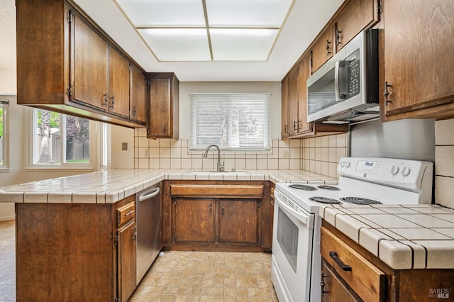 kitchen featuring a peninsula, tile counters, a sink, backsplash, and stainless steel appliances