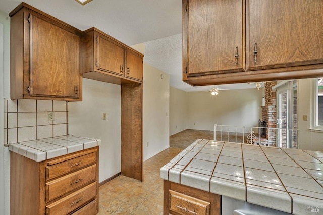 kitchen with brown cabinetry, baseboards, ceiling fan, tile countertops, and backsplash