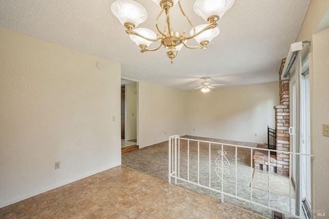 spare room featuring a brick fireplace, a textured ceiling, stone finish flooring, and ceiling fan with notable chandelier