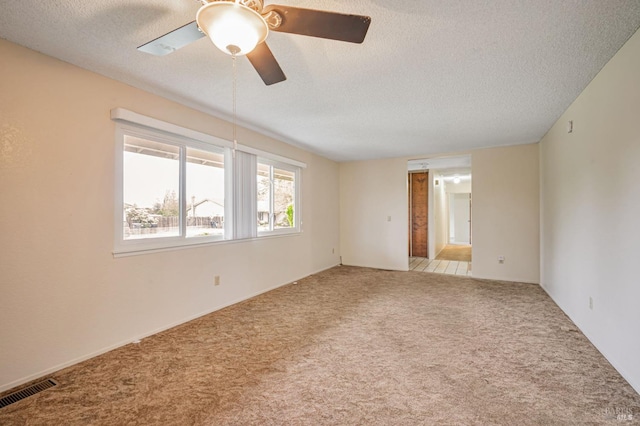 carpeted empty room with visible vents, a textured ceiling, and ceiling fan