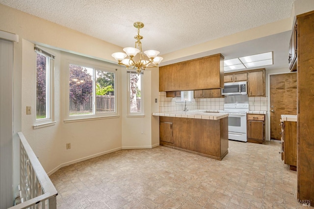 kitchen with a peninsula, tile countertops, stainless steel microwave, brown cabinets, and electric stove