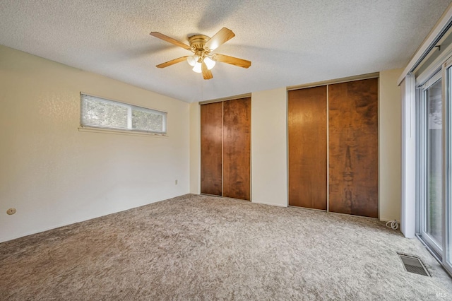 unfurnished bedroom featuring visible vents, carpet floors, two closets, a textured ceiling, and a ceiling fan