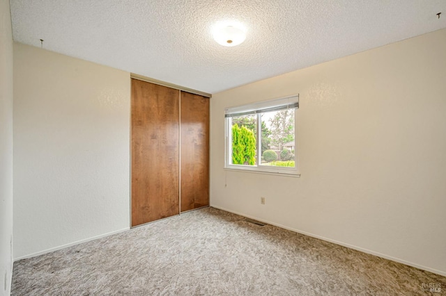 unfurnished bedroom featuring a textured ceiling, visible vents, baseboards, a closet, and carpet