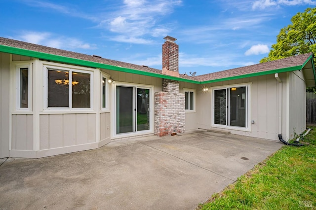 rear view of property featuring a patio, a shingled roof, board and batten siding, and a chimney