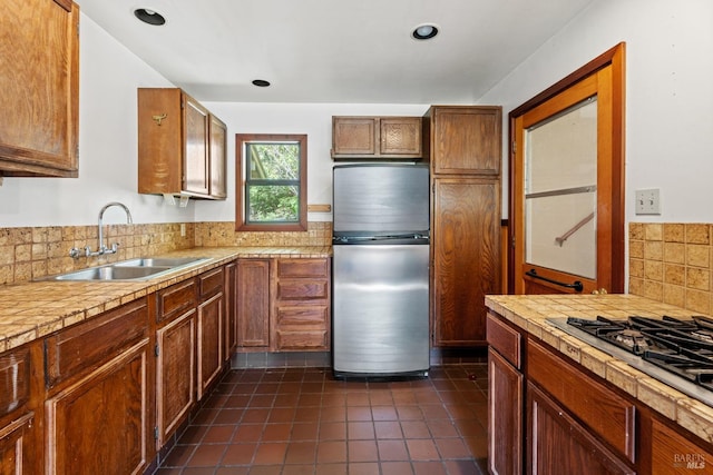 kitchen featuring a sink, decorative backsplash, light countertops, dark tile patterned floors, and appliances with stainless steel finishes