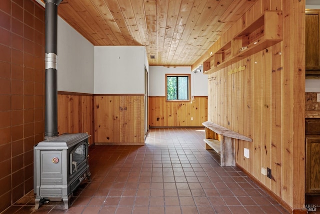 bonus room with wood walls, a wood stove, wood ceiling, dark tile patterned flooring, and wainscoting