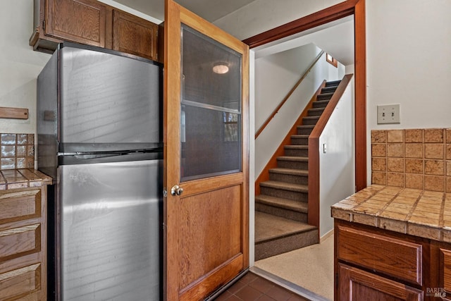 kitchen featuring tasteful backsplash, tile counters, dark tile patterned flooring, and freestanding refrigerator