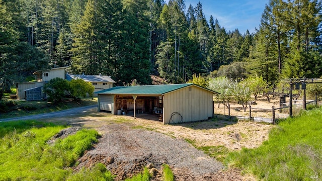 garage featuring fence, a view of trees, a carport, and driveway