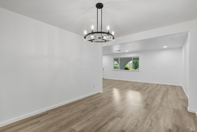 empty room featuring recessed lighting, an inviting chandelier, light wood finished floors, and baseboards