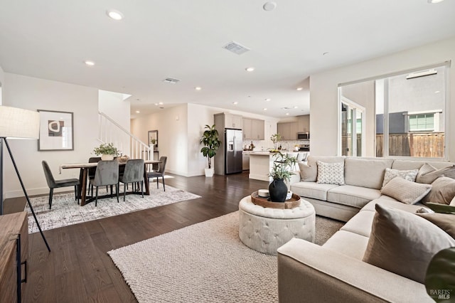 living area with baseboards, visible vents, dark wood-style floors, and stairs