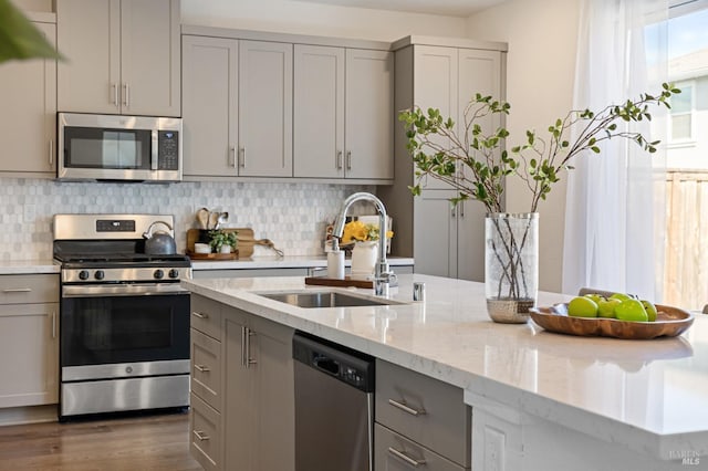 kitchen featuring dark wood-style floors, a sink, decorative backsplash, gray cabinetry, and appliances with stainless steel finishes