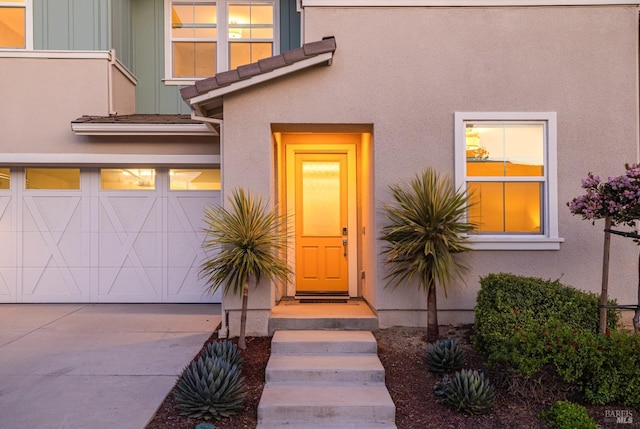 view of exterior entry with board and batten siding, driveway, and stucco siding