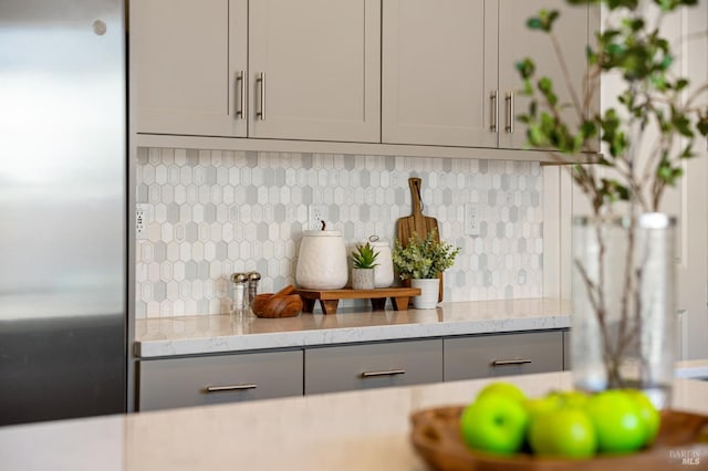 interior details featuring backsplash, light stone countertops, gray cabinets, and stainless steel refrigerator