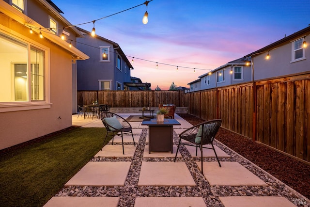 patio terrace at dusk featuring outdoor dining space, a lawn, and a fenced backyard
