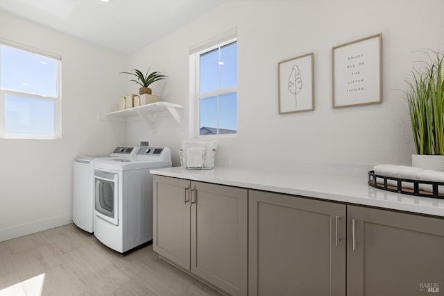 washroom featuring baseboards, washing machine and clothes dryer, cabinet space, and plenty of natural light