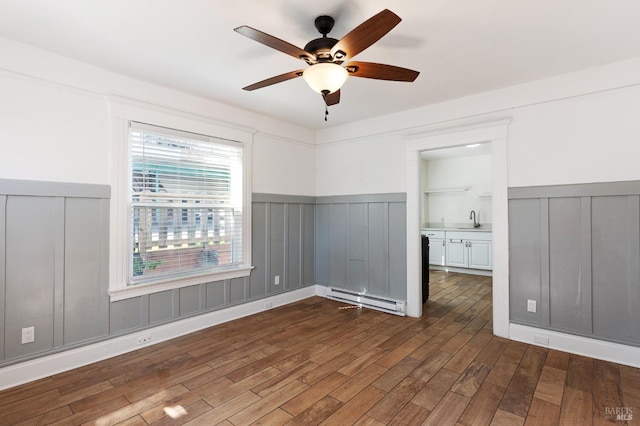 spare room with a baseboard heating unit, wainscoting, ceiling fan, and a decorative wall