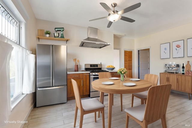 kitchen with wall chimney range hood, a wealth of natural light, appliances with stainless steel finishes, and a ceiling fan