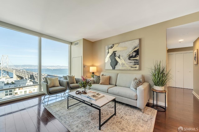 living area featuring floor to ceiling windows, a water view, and wood finished floors