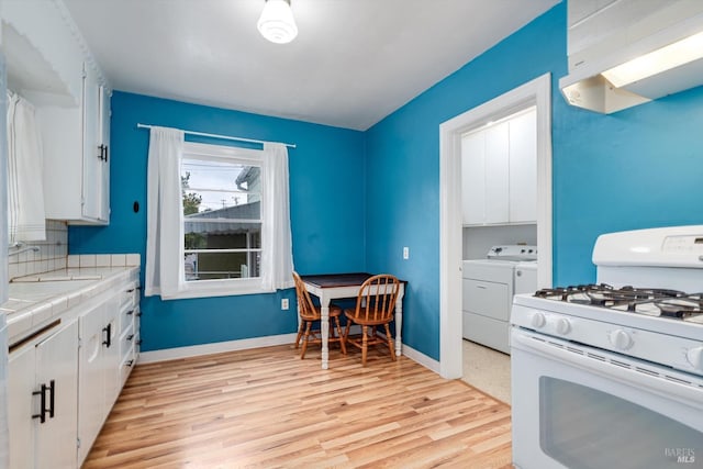 kitchen featuring white cabinets, washing machine and dryer, light wood-style floors, tile counters, and white range with gas stovetop