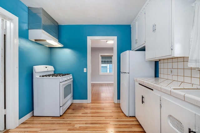 kitchen featuring tasteful backsplash, tile counters, white appliances, light wood-style flooring, and white cabinetry