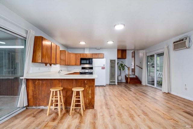 kitchen featuring an AC wall unit, gas range oven, freestanding refrigerator, black microwave, and light wood-style flooring