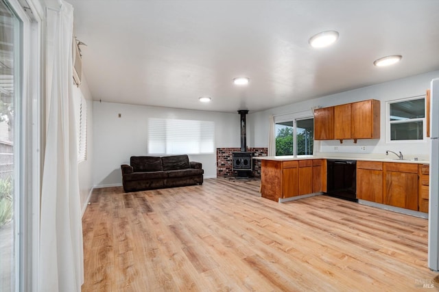 kitchen featuring brown cabinets, open floor plan, dishwasher, a wood stove, and light countertops