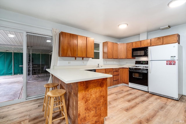 kitchen with a peninsula, freestanding refrigerator, gas range oven, black microwave, and brown cabinetry