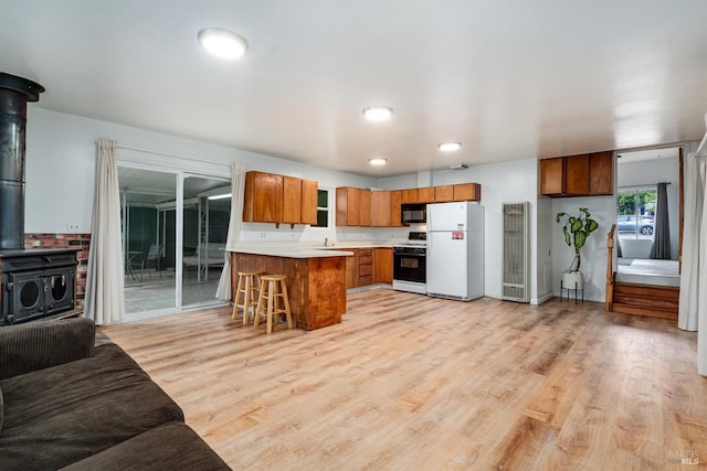 kitchen with a wood stove, freestanding refrigerator, black microwave, gas stove, and brown cabinetry