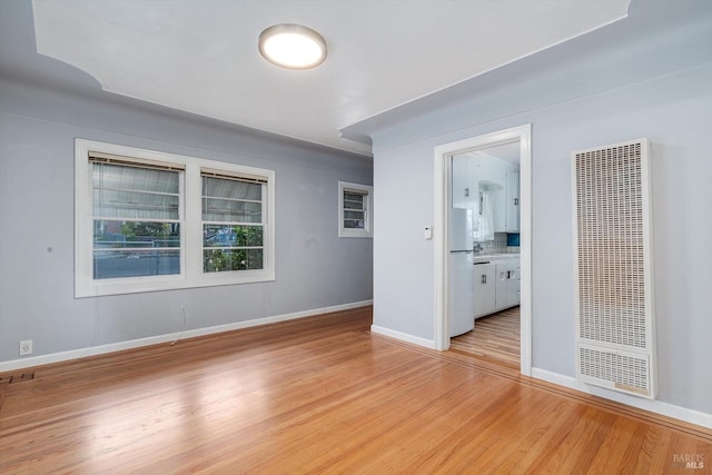 spare room with light wood finished floors, baseboards, and a heating unit
