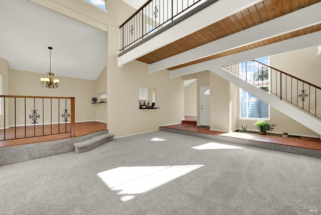 unfurnished living room featuring baseboards, carpet, a notable chandelier, beamed ceiling, and stairway