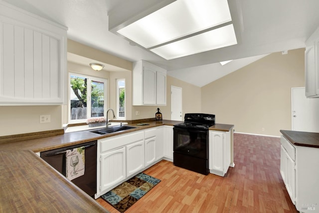 kitchen with white cabinets, a peninsula, a sink, light wood-style floors, and black appliances