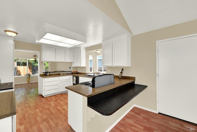 kitchen with dark countertops, a sink, light wood-type flooring, a peninsula, and white cabinetry
