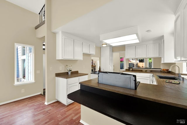 kitchen with white cabinets, a peninsula, light wood-style flooring, a sink, and dark countertops