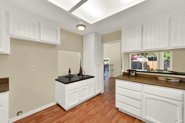 kitchen featuring light wood-type flooring, dark countertops, and white cabinetry