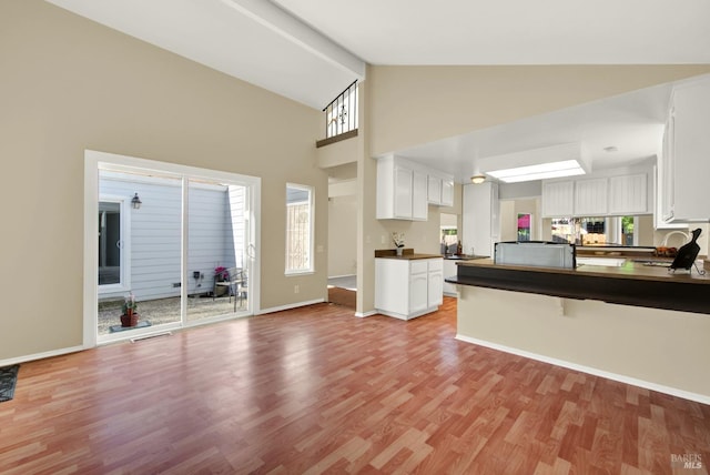 kitchen featuring light wood finished floors, dark countertops, baseboards, high vaulted ceiling, and white cabinetry