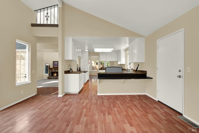 kitchen with high vaulted ceiling, dark countertops, light wood-style floors, a peninsula, and white cabinetry