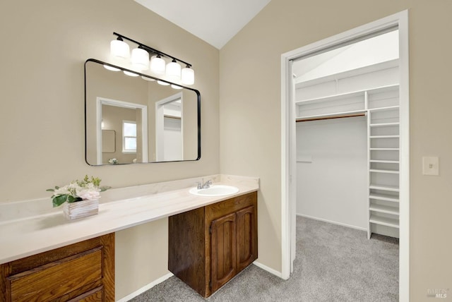 bathroom with a walk in closet, vaulted ceiling, baseboards, and vanity