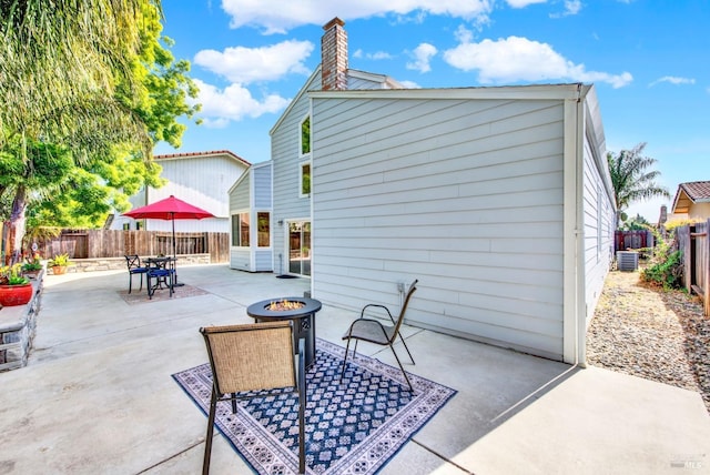 back of house with a chimney, a fenced backyard, central air condition unit, a patio, and a fire pit