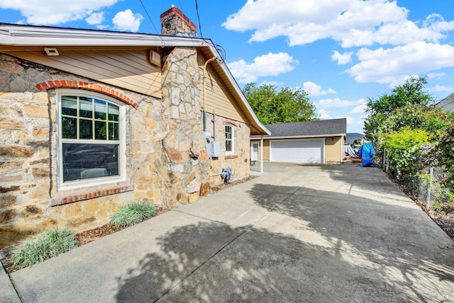 view of property exterior featuring a detached garage, an outbuilding, stone siding, and a chimney
