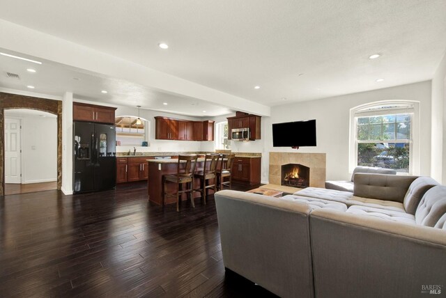 living area featuring dark wood-style floors, arched walkways, a tiled fireplace, visible vents, and recessed lighting