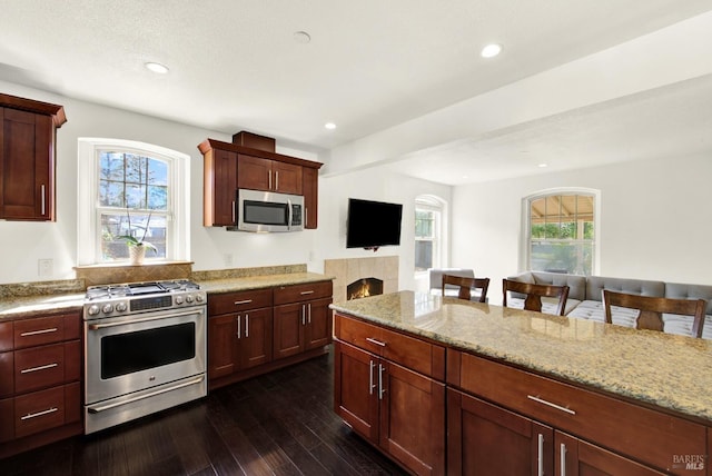 kitchen featuring recessed lighting, a tile fireplace, dark wood-style floors, light stone counters, and appliances with stainless steel finishes