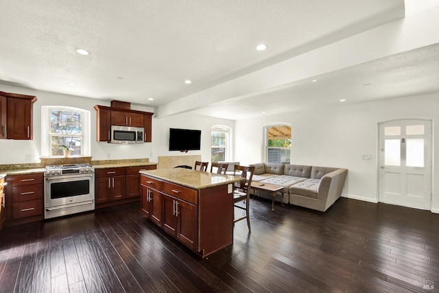 kitchen with light stone counters, a kitchen island, a kitchen bar, appliances with stainless steel finishes, and open floor plan