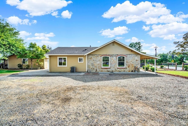 ranch-style home with stone siding, roof with shingles, and central AC unit