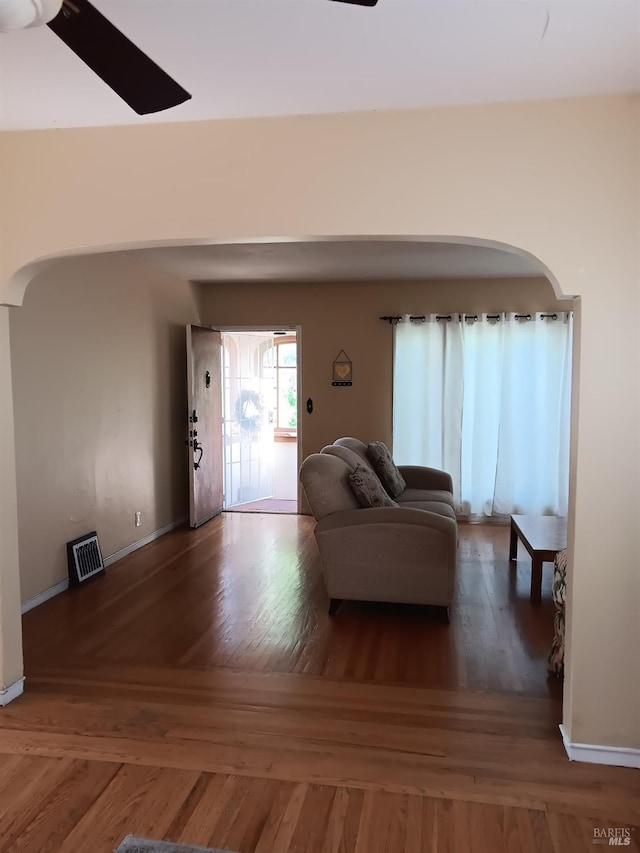 living room featuring arched walkways, baseboards, visible vents, and wood finished floors