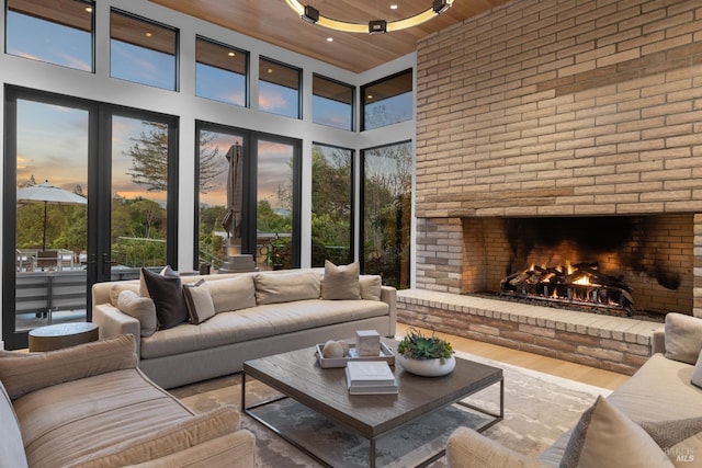 living room featuring a fireplace, a towering ceiling, wooden ceiling, and brick wall